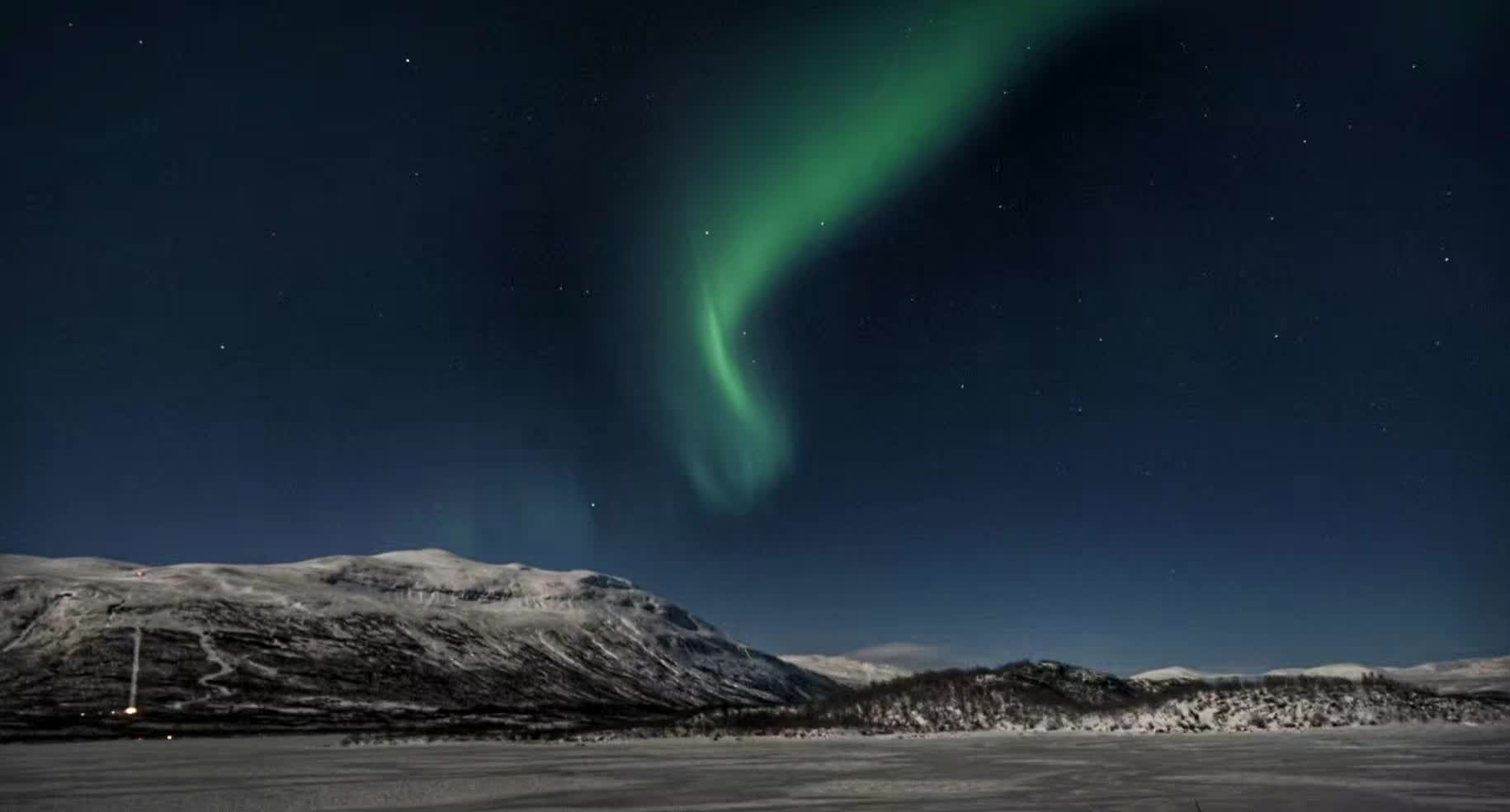 Aurora above a snow-covered landscape in Abisko, photographed by Shule Wang in 2018.